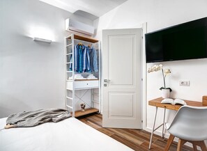 A bedroom with a bed, a desk with a chair, a TV mounted on the wall, a wardrobe, and a potted orchid. - Sorrento Lux Suites - Oro (Sorrento)