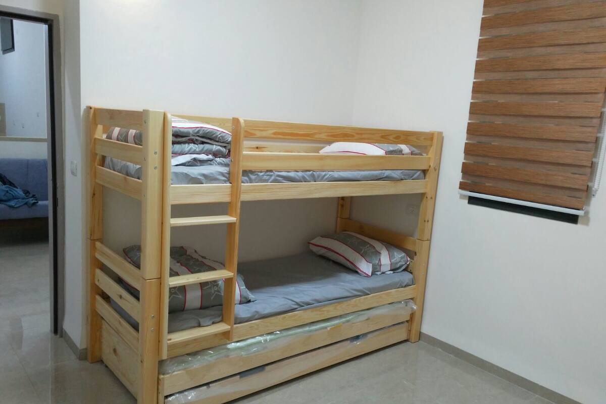 A bunk bed with a ladder, a small drawer, and a window with blinds.