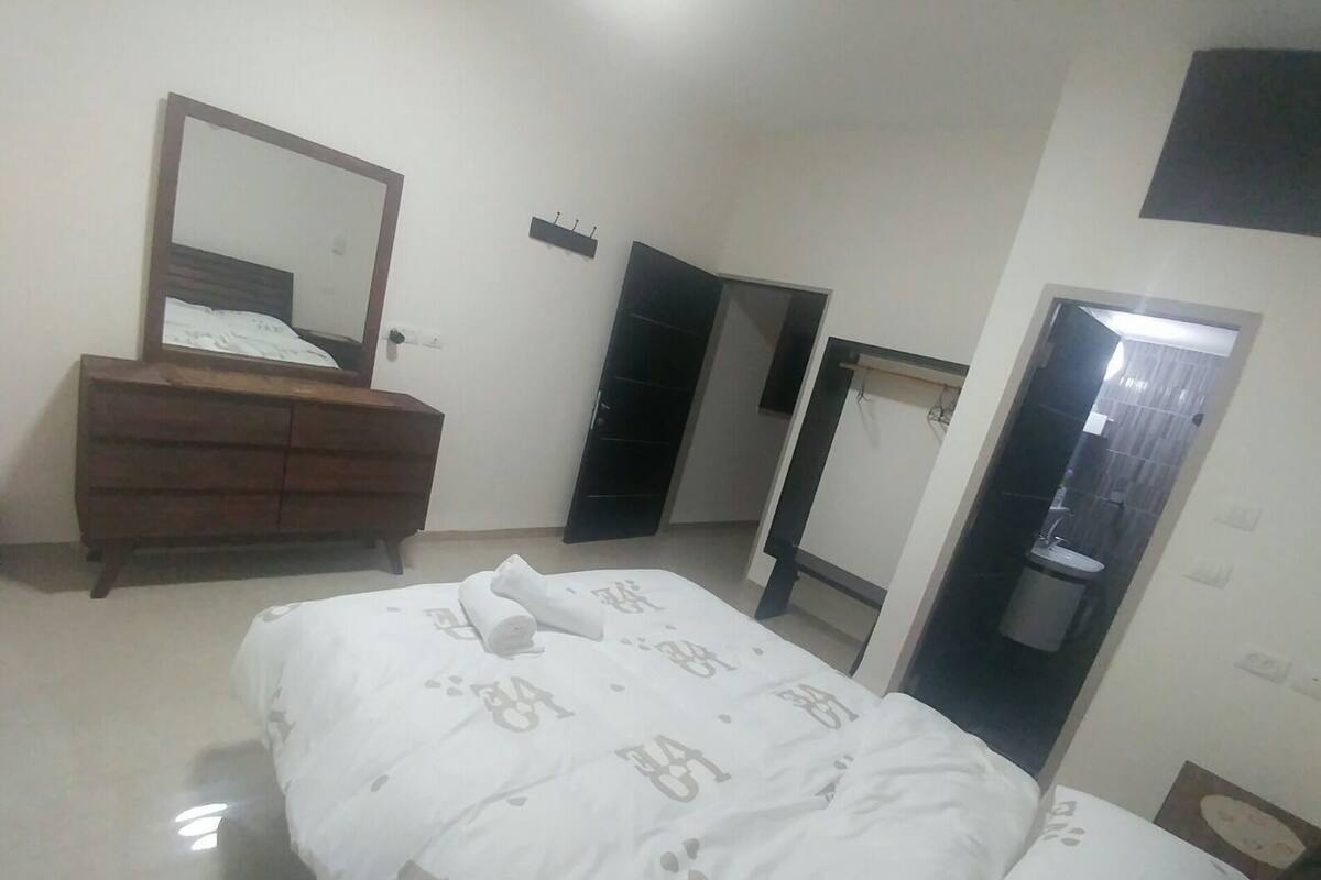 A bedroom with a bed, a wooden dresser, a mirror, and a wardrobe.