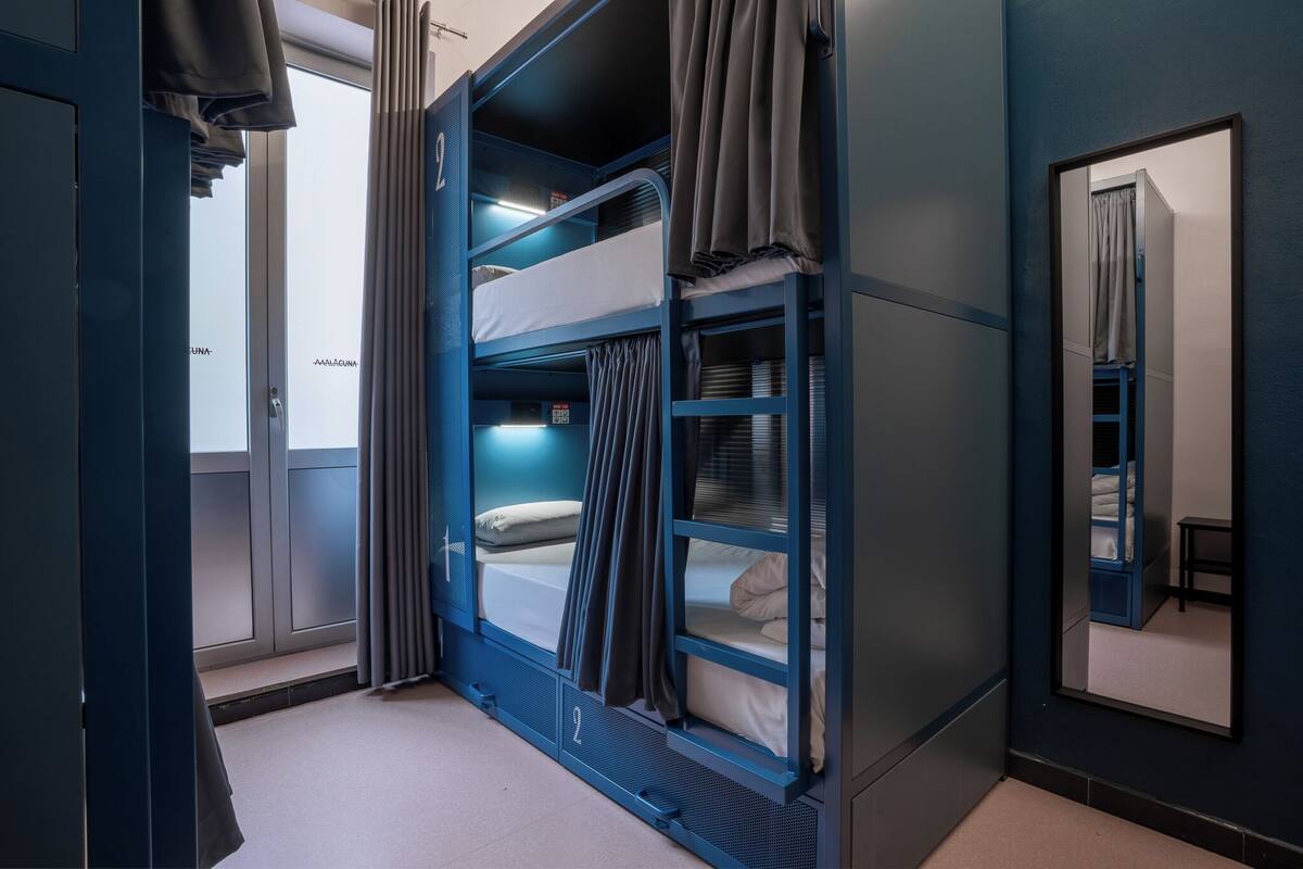 Een slaapkamer met een stapelbed, raam, gordijnen en een spiegel aan de muur.