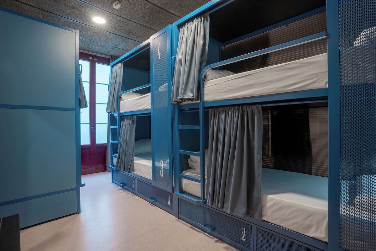 Een studentenkamer met stapelbedden, een deur en een raam.
