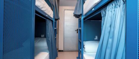 A narrow corridor with bunk beds on either side, a door at the end, and a ventilation system on the ceiling.