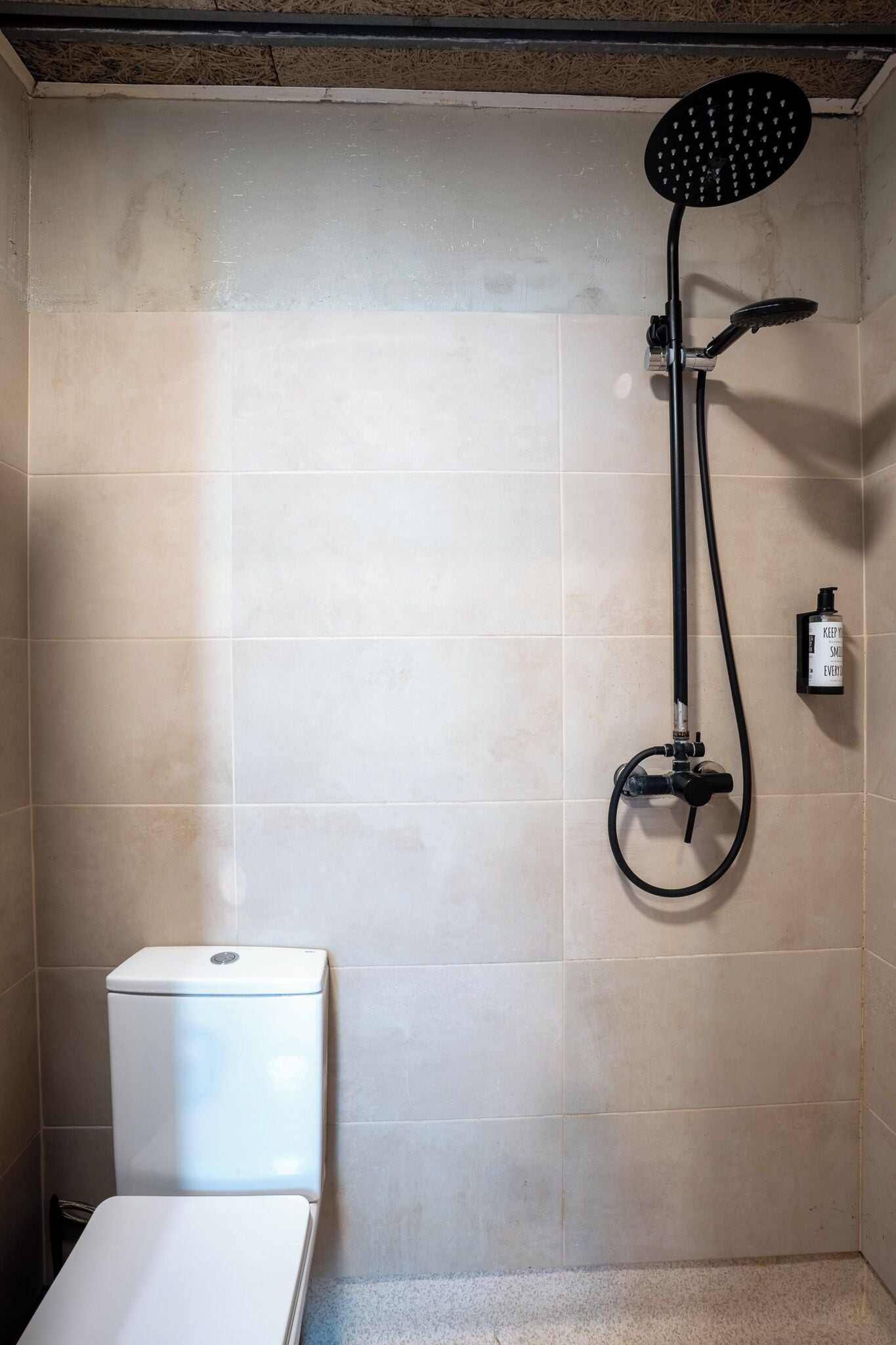 A bathroom with a shower, toilet, and a bottle of hand soap on the wall.