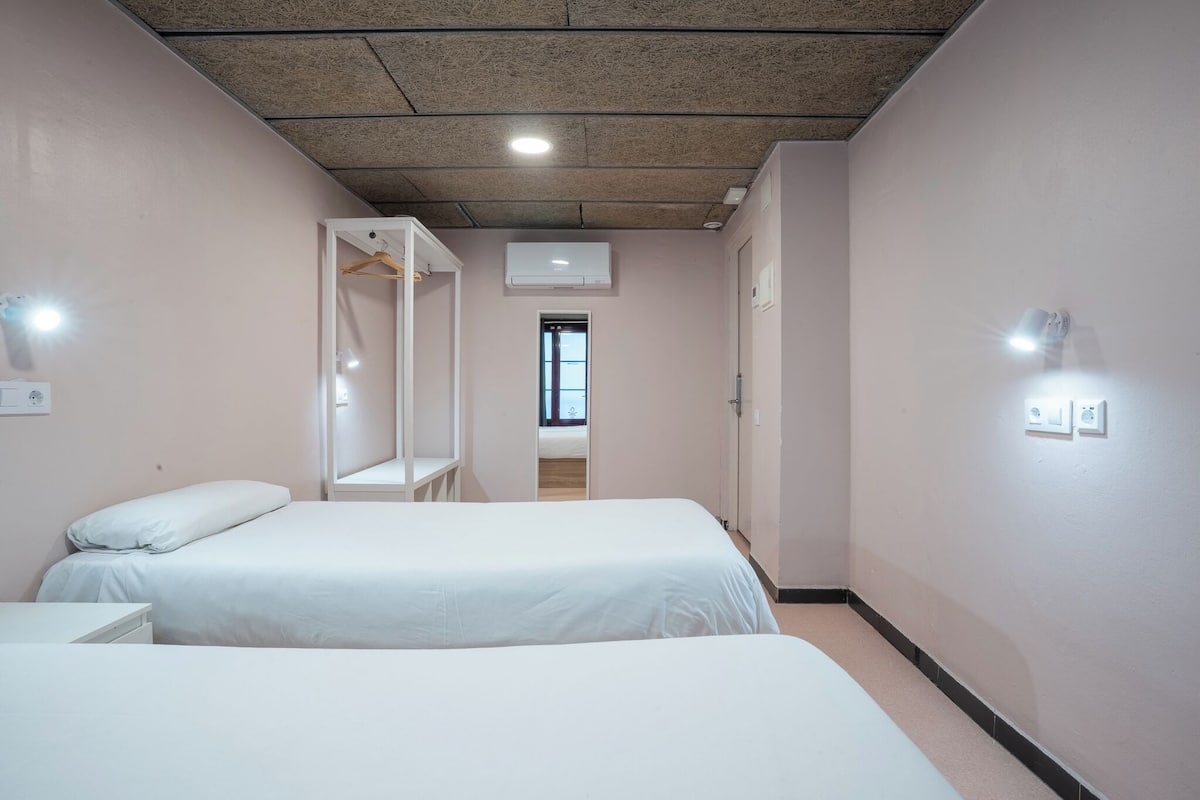 Een hotelkamer met twee bedden, een kledingkast, een spiegel en een deur naar een andere kamer.