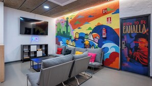 Un área de descanso moderna con un mural colorido, un televisor de pantalla plana y asientos cómodos.
