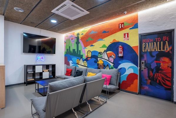 Un área de descanso moderna con un mural colorido, un televisor de pantalla plana y asientos cómodos.