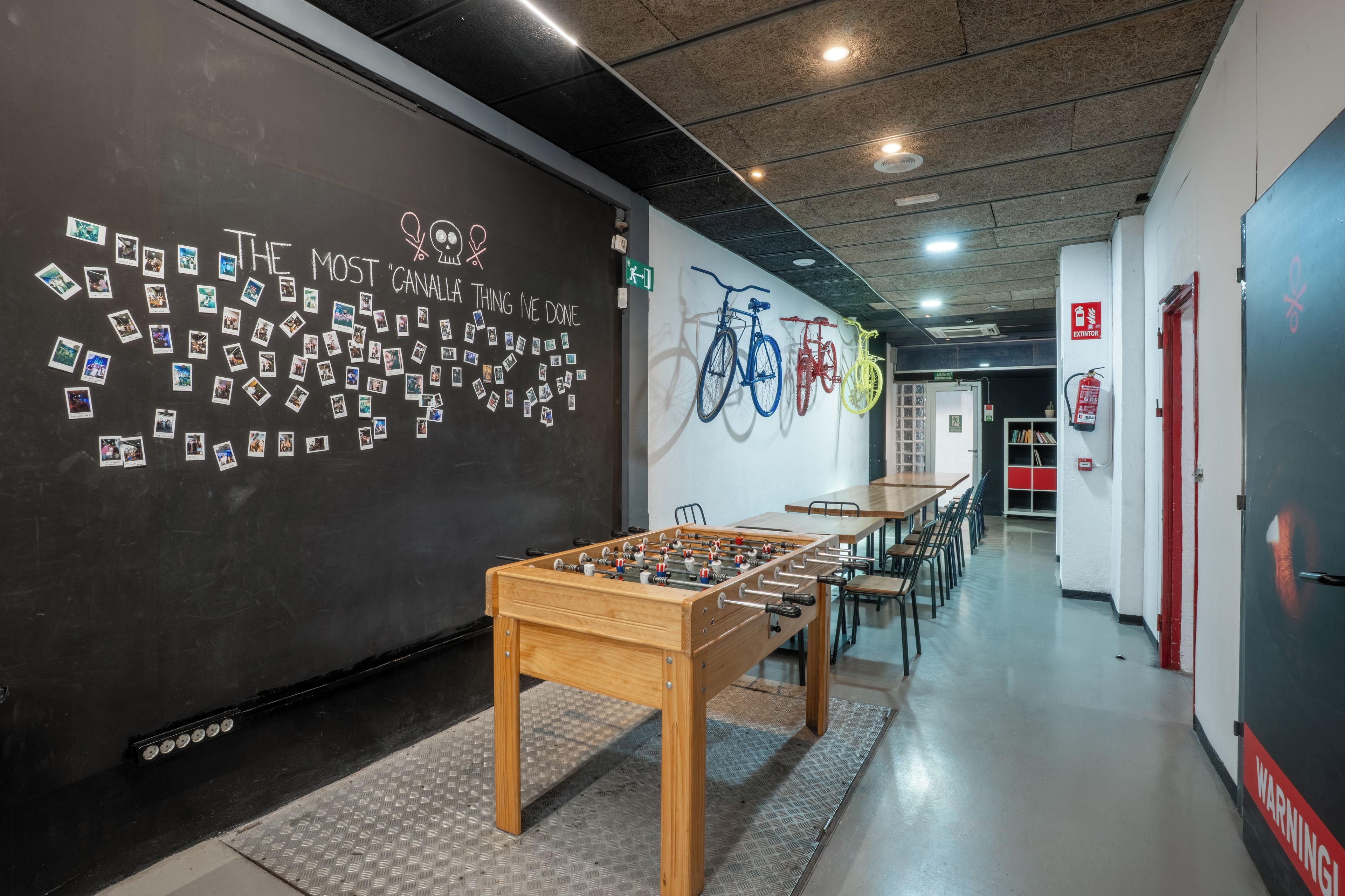 A hallway with a foosball table, bicycles mounted on the wall, and a blackboard with photos.