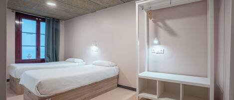 A hotel room with two single beds, a white wardrobe, and a small bench.