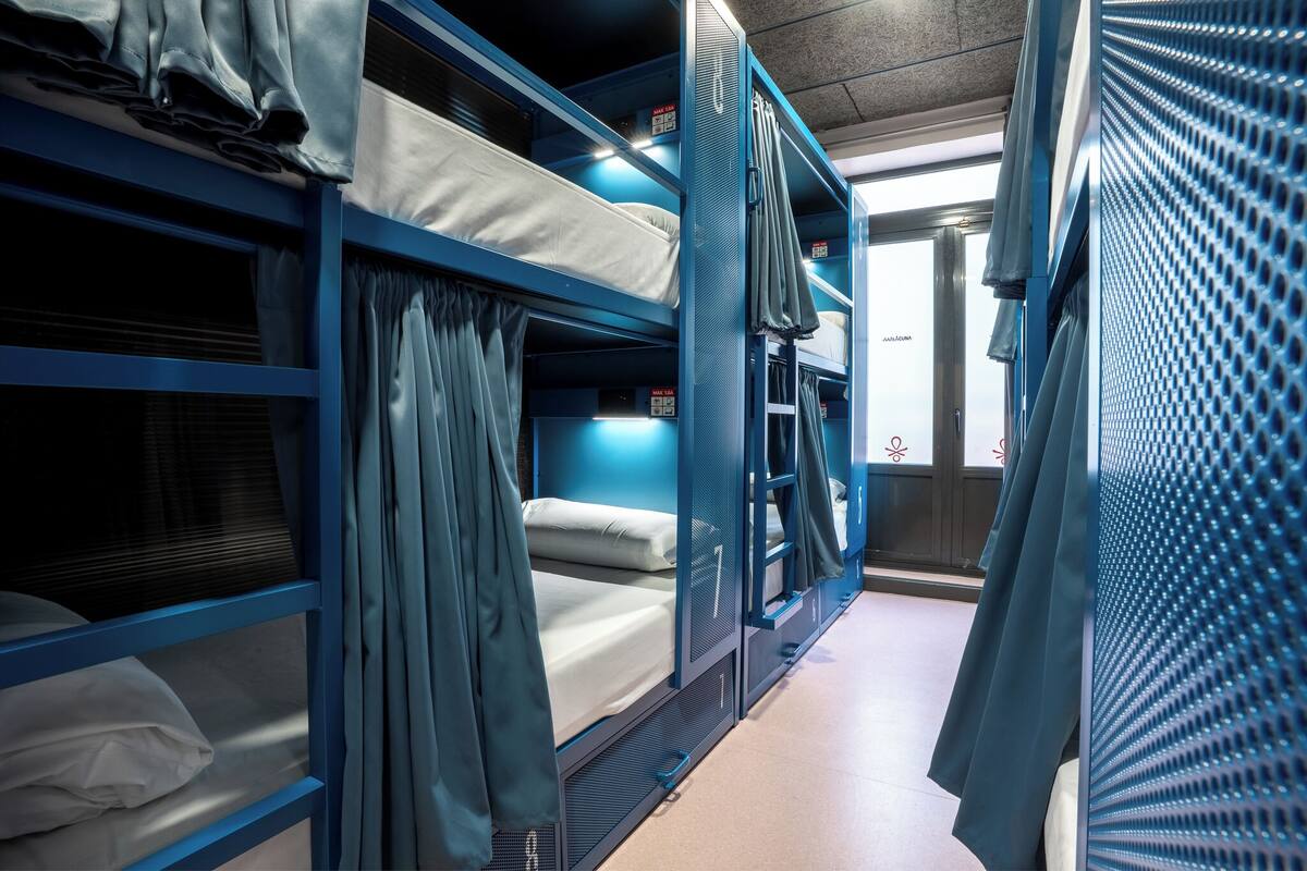 Een treinwagon met blauwe slaapplaatsen, gordijnen en een raam met uitzicht.