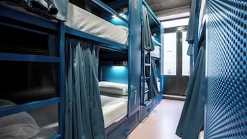A train compartment with blue bunk beds, curtains, and a window with a view of the outside.