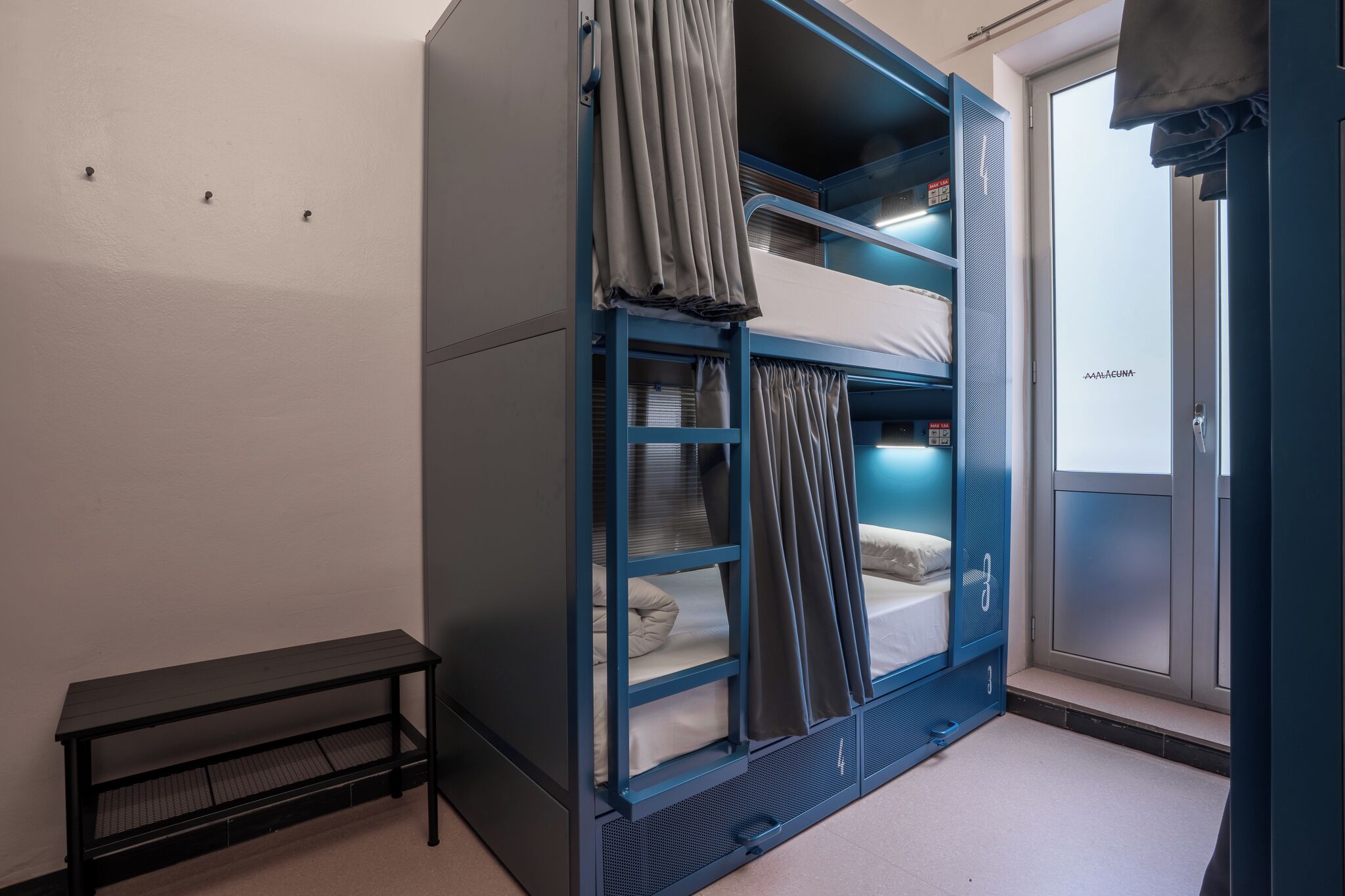 A dormitory room with bunk beds, a small table, and a door with a frosted glass panel.