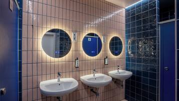 Eine Toilette mit drei Waschbecken, jeweils mit einem Spiegel darüber. Die Wände sind mit hellen und dunklen Fliesen in einem Gittermuster versehen.