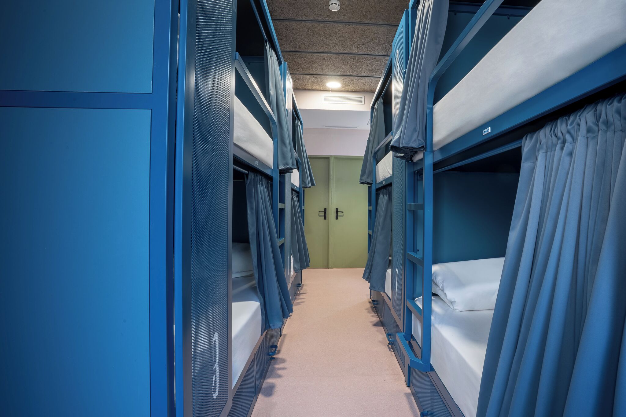 A narrow corridor with bunk beds on both sides, a carpeted floor, and a door at the end.