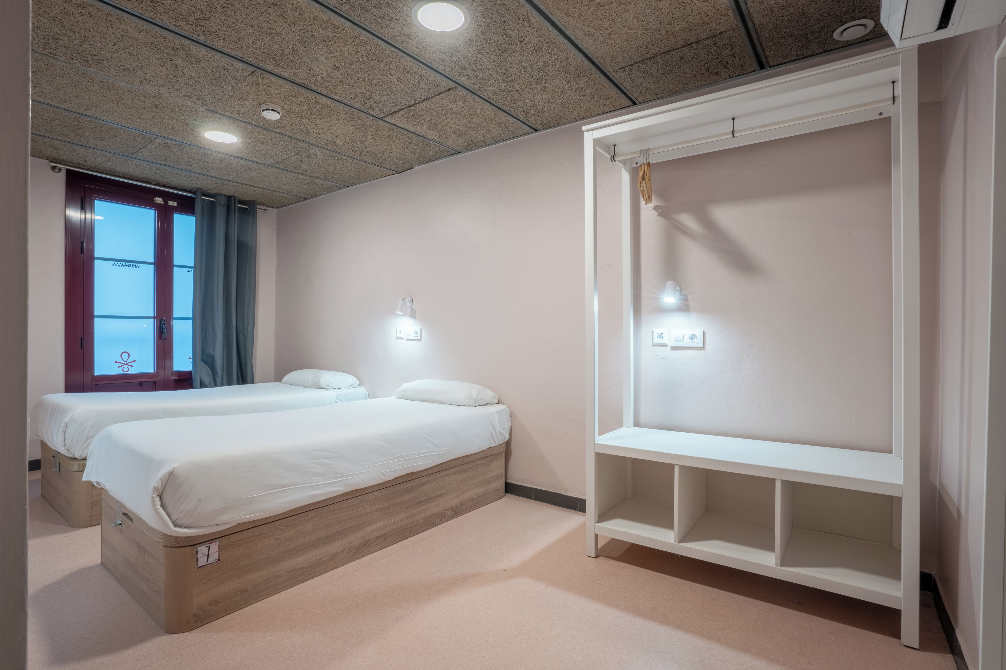 A hotel room with two beds, a wardrobe, and a window with curtains.
