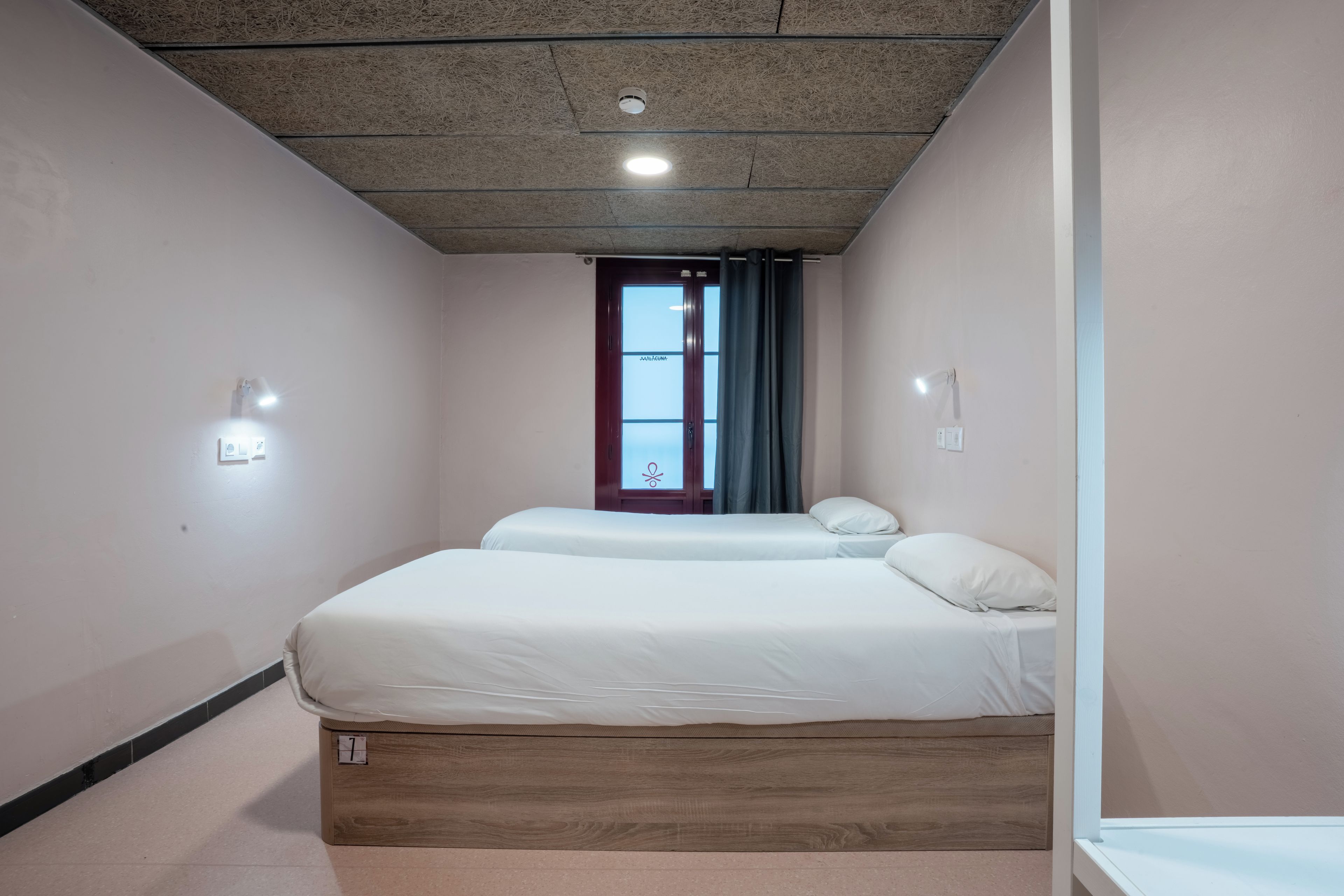 Habitación de hotel con dos camas, una ventana con cortinas, una lámpara de techo y una luz en la pared.