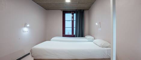 Habitación de hotel con dos camas, una ventana con cortinas, una lámpara de techo y una luz en la pared.