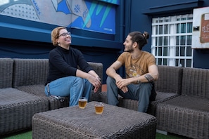 Dos personas sentadas en muebles de mimbre con bebidas sobre una mesa.
