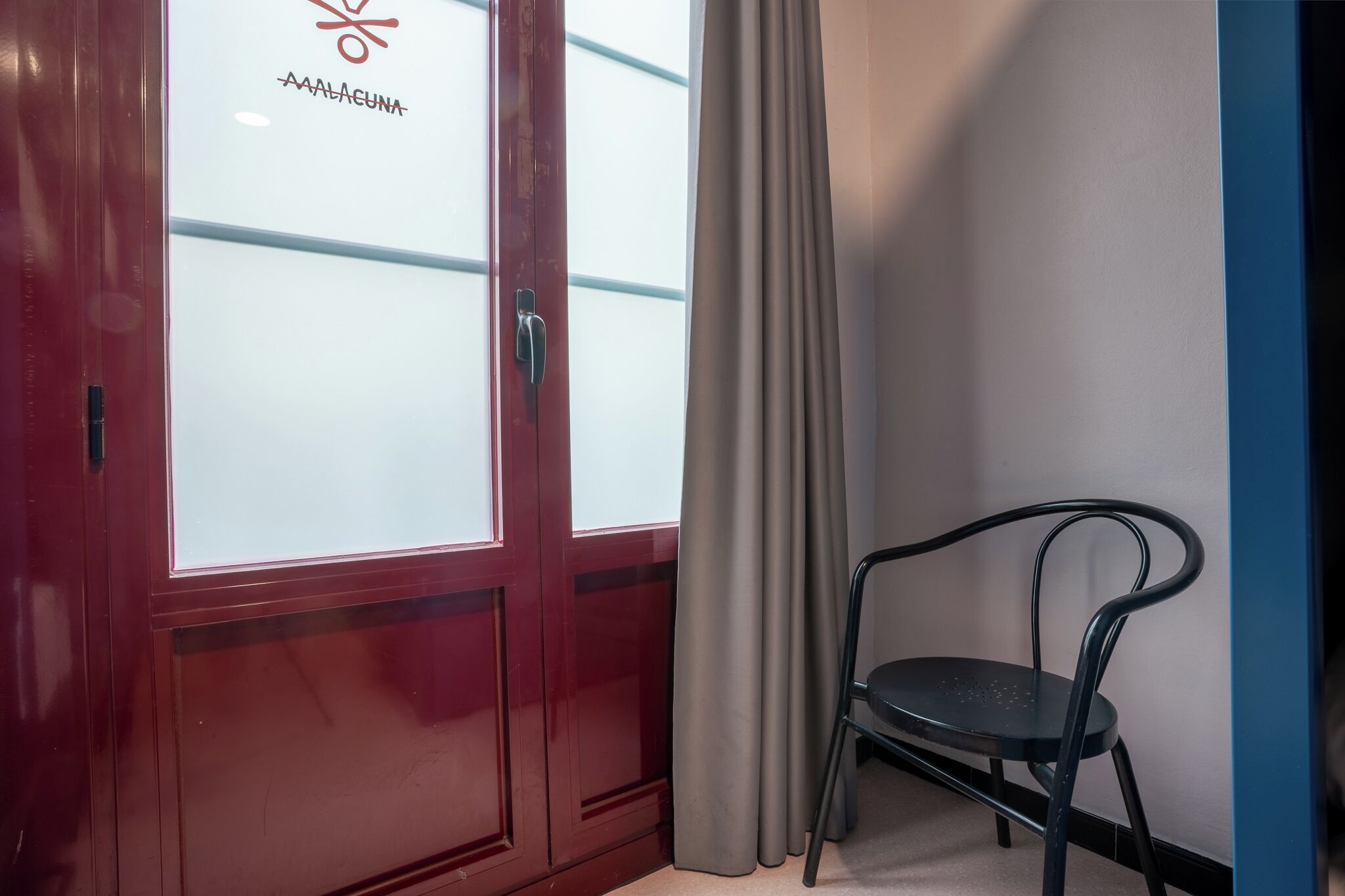 Una habitación con una puerta roja, una silla negra y una cortina.