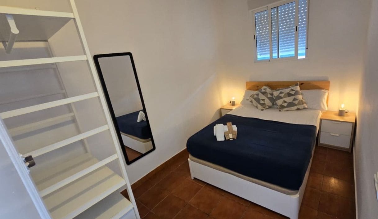 A bedroom with a bed, bedside tables, a mirror, and a window with blinds.