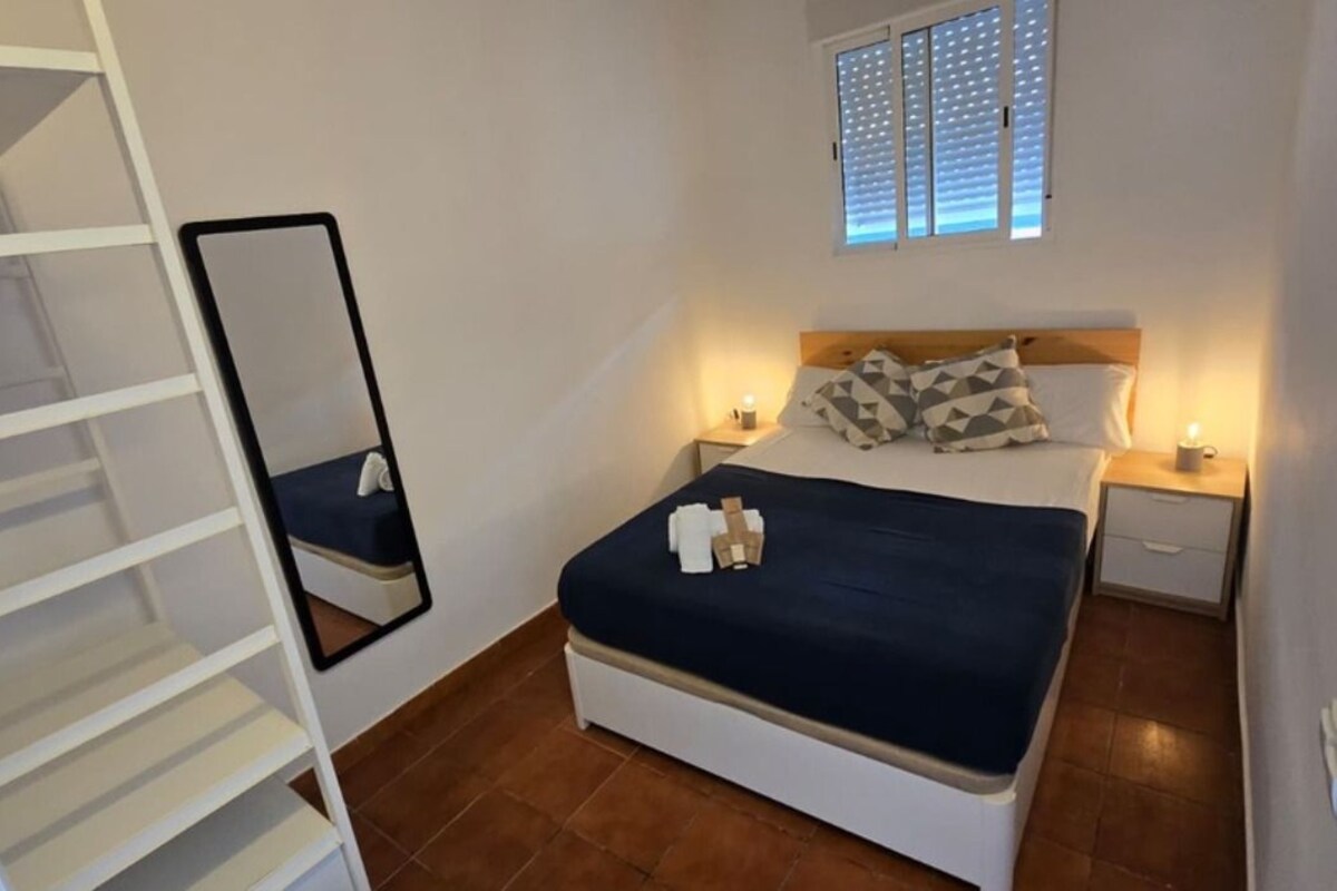 A bedroom with a bed, bedside tables, a mirror, and a window with blinds.