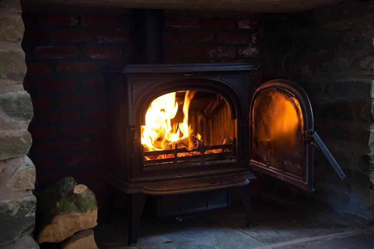 Una estufa de leña con la puerta abierta, mostrando un fuego en su interior.