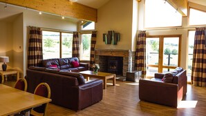 A spacious living room with a fireplace, leather sofas, wooden flooring, and large windows offering a view of the outdoors. - Forbes of Kingennie Country Resort (Dundee)
