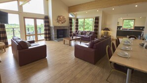 A spacious living area with a fireplace, leather sofas, a dining table set for four, and large windows offering a view of the outdoors. - Forbes of Kingennie Country Resort (Dundee)