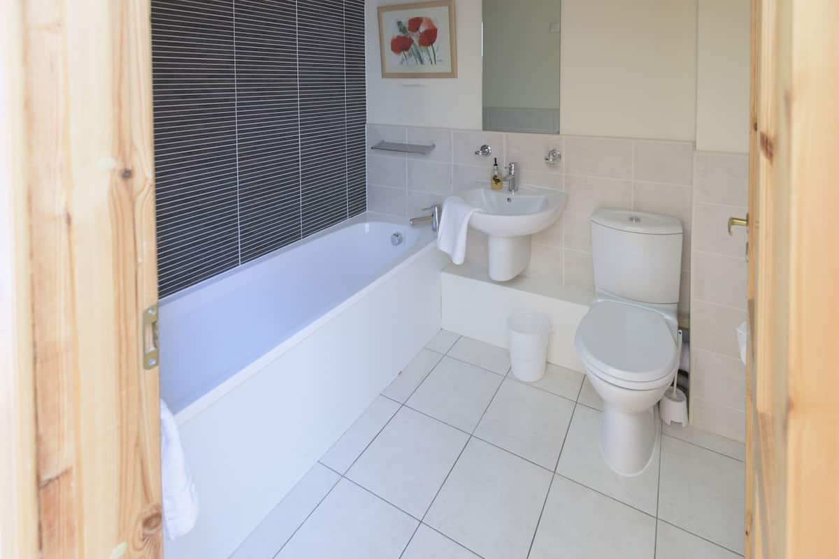 Un baño con bañera, lavabo, inodoro y una ventana con persianas.