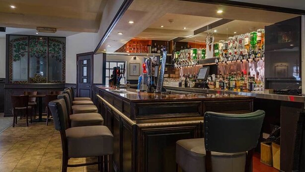 Una zona de bar con una barra alargada, varios taburetes y una amplia selección de botellas y vasos.