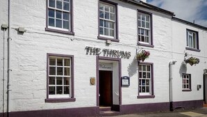 Un edificio blanco con el cartel "THE THRUMS" y una entrada acogedora.