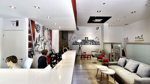 A modern interior with a long white counter, seating area with a sofa and chairs, and a wall with black and white artwork. - Clá Hotel Boutique (Teruel)
