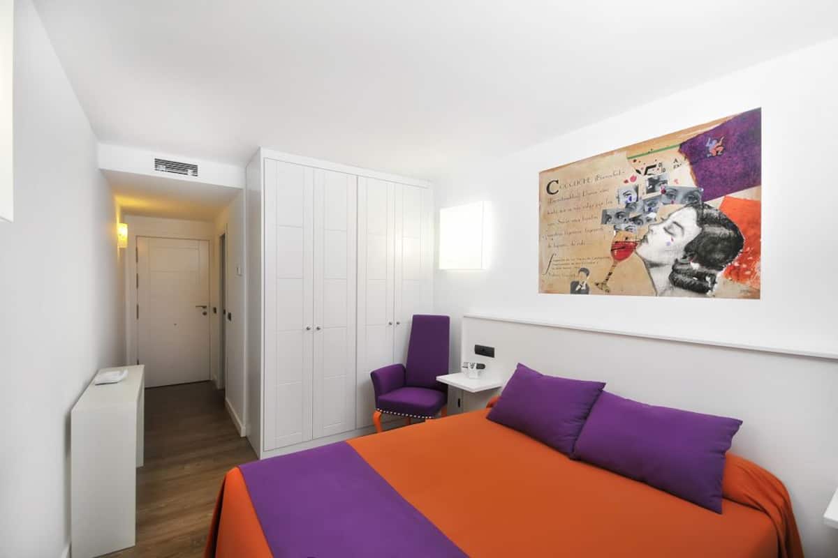 Una habitación de hotel con cama, una silla, un escritorio y un armario.