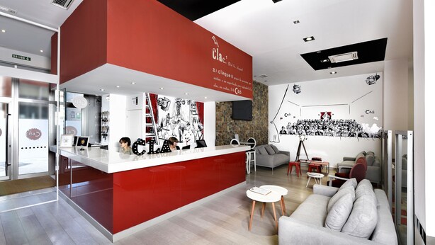 A modern interior with a red and white color scheme, featuring a kitchen area with a counter and stools, a seating area with a sofa and a coffee table, and a wall with black and white artwork. - Clá Hotel Boutique (Teruel)