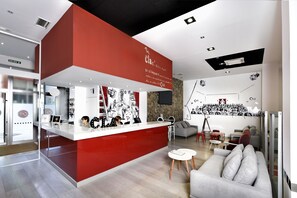 A modern interior with a red and white color scheme, featuring a kitchen area with a counter and stools, a seating area with a sofa and a coffee table, and a wall with black and white artwork. - Clá Hotel Boutique (Teruel)