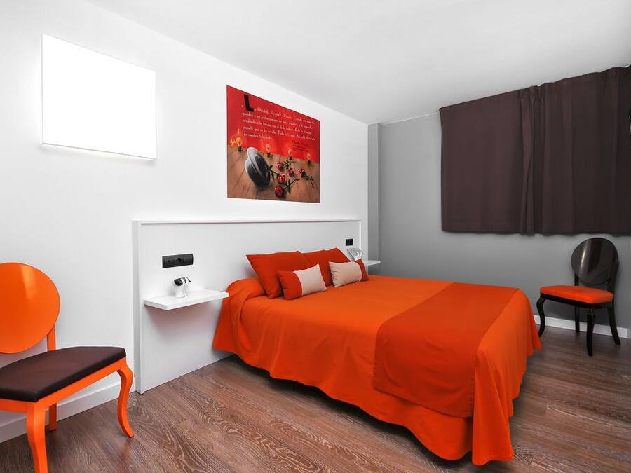 Una camera d'albergo moderna con un letto grande, un comodino, una sedia e un'ampia finestra con tende.