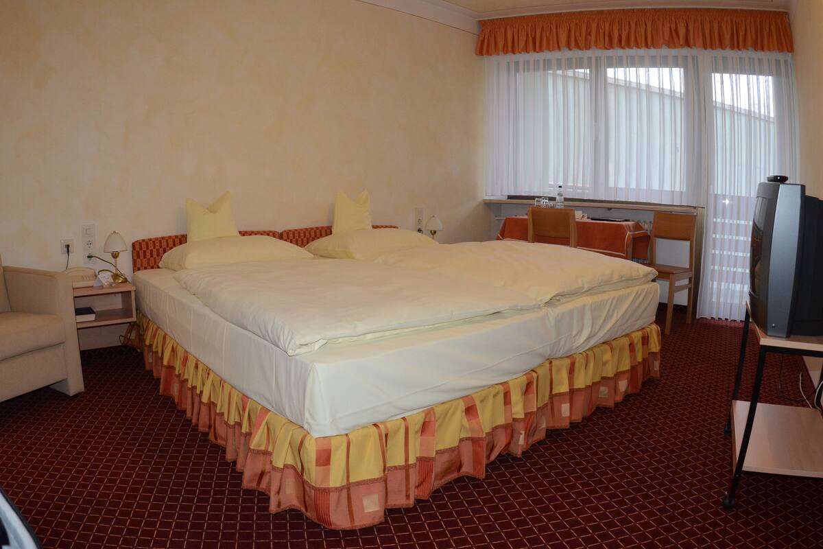 Ein Hotelzimmer mit einem großen Bett, einem Schreibtisch, einem Stuhl, einem Fernseher und einem Fenster mit Vorhängen.