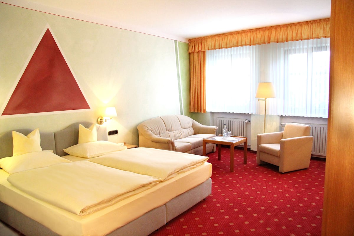Ein Hotelzimmer mit einem großen Bett, zwei Sesseln, einem kleinen Tisch und einer Lampe.