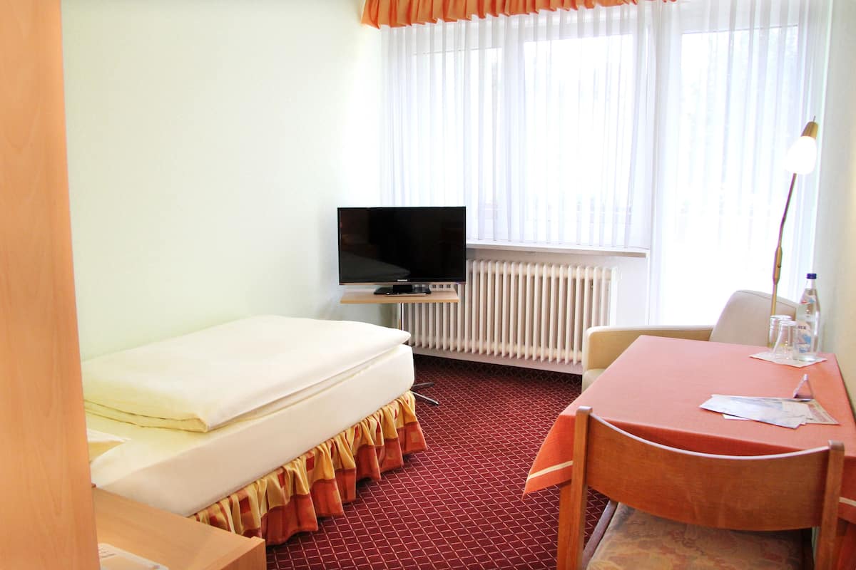 Ein Hotelzimmer mit Bett, Fernseher, Tisch mit Stühlen und einem Fenster mit Vorhängen.