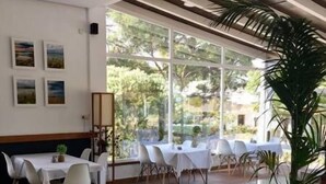 A dining area with white tables and chairs, large windows with a view of greenery, and a patterned rug on the floor. - Hotel Marisma Sancti Petri (Chiclana de la Frontera)