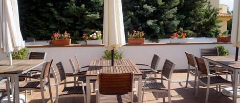 An outdoor patio with wooden tables and chairs, white umbrellas, and potted plants.