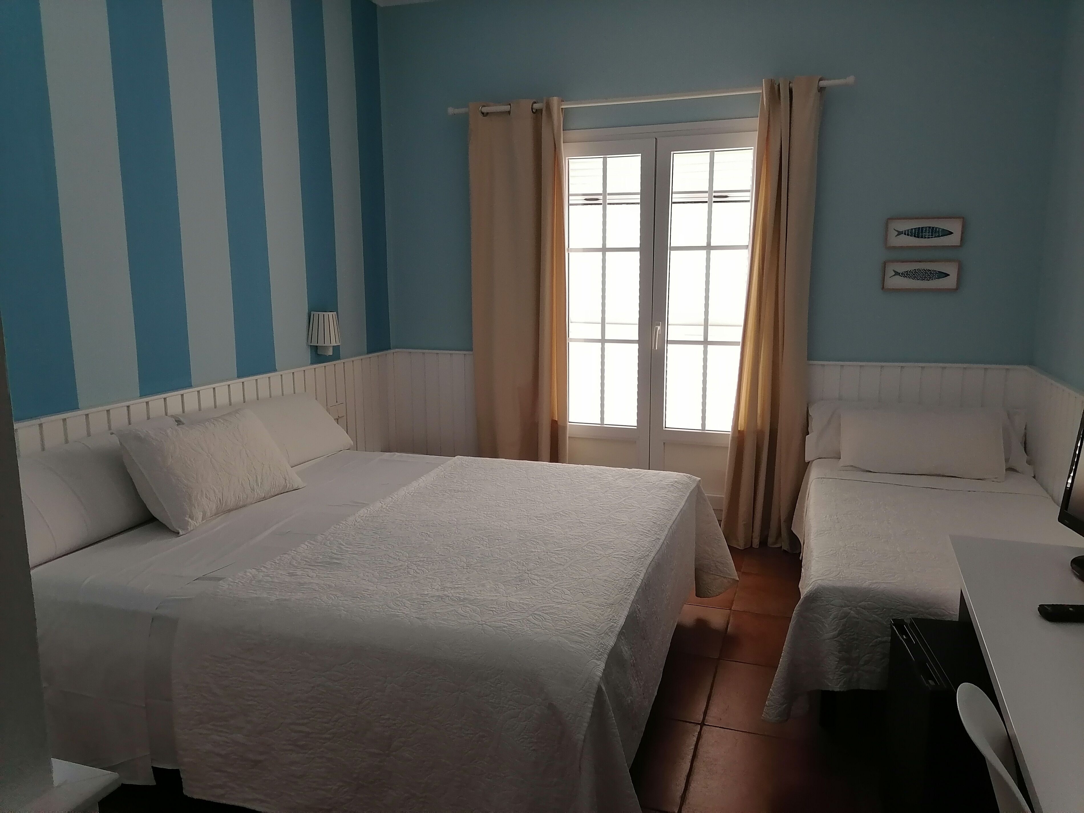 Hotellihuone, jossa on kaksi sänkyä, ikkuna, jossa on verhot, lamppu ja seinä, jossa on kalan kuva.