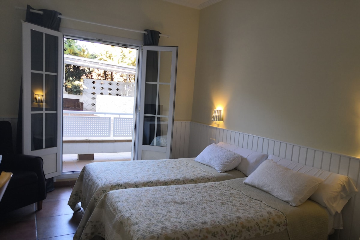 A bedroom with two beds, a balcony, and a sliding door.