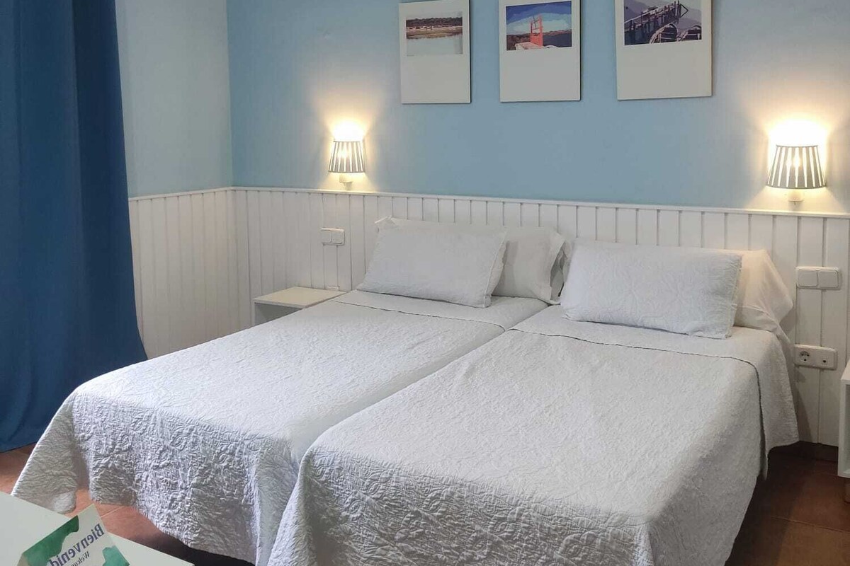 A double bed with white bedding in a room with light blue walls and two bedside lamps.