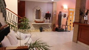A lobby with a staircase, a white sofa, a large mirror, a vase, and a reception desk. - Hotel Marisma Sancti Petri (Chiclana de la Frontera)