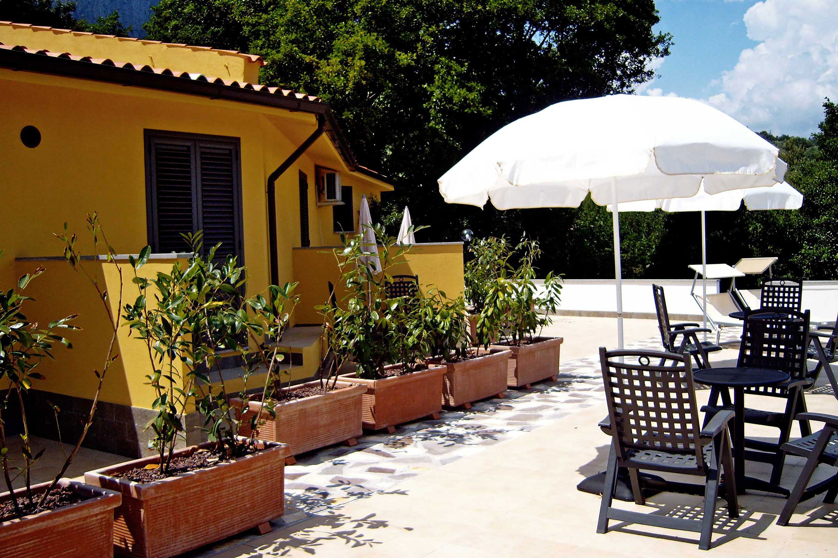 Un patio exterior con plantas en macetas, mobiliario de exterior y una sombrilla blanca.