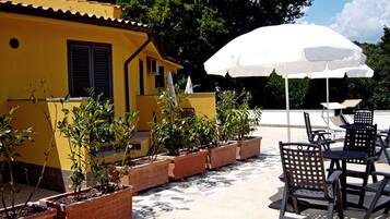 Un patio exterior con plantas en macetas, mobiliario de exterior y una sombrilla blanca.