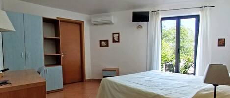 A bedroom with a bed, a desk, a wardrobe, a window with curtains, and a small table.