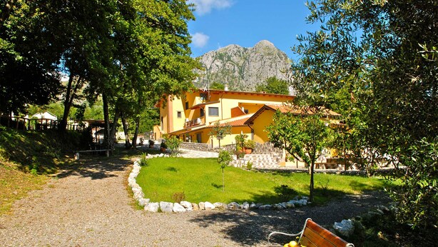 A building with a yellow facade, a paved pathway, and a bench with fruit. - Verdeblu House (San Giovanni a Piro)