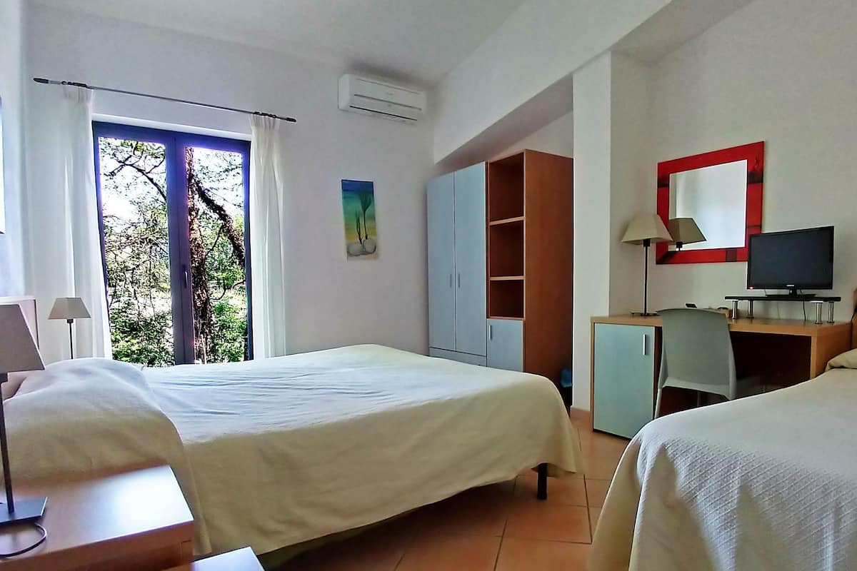 A hotel room with two beds, a desk with a lamp, a television, and a wardrobe.