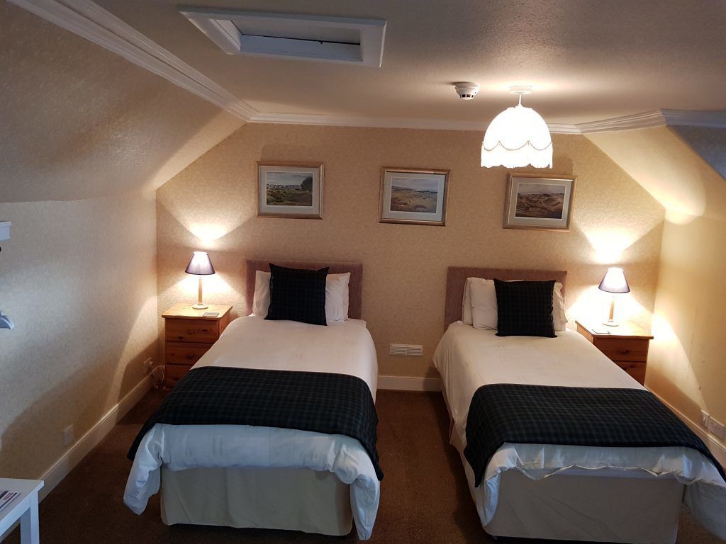 A twin room with two beds, each with a pillow and a lamp on a bedside table.